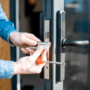 Mains d'une personne installant un cylindre de serrure argenté avec un tournevis sur une porte noire.