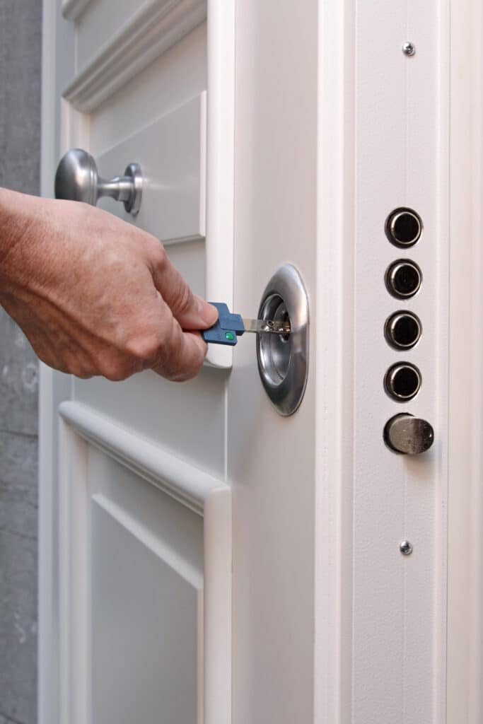 Main insérant une clé de sécurité bleue dans la serrure d'une porte blindée blanche. Les pênes sont visibles sur le côté.