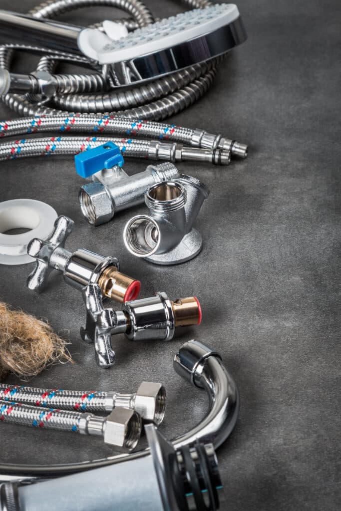 Équipements de plomberie sur fond sombre : flexible de douche, raccords chromés, robinets, ruban téflon et filasse. Idéal pour réparation salle de bain.